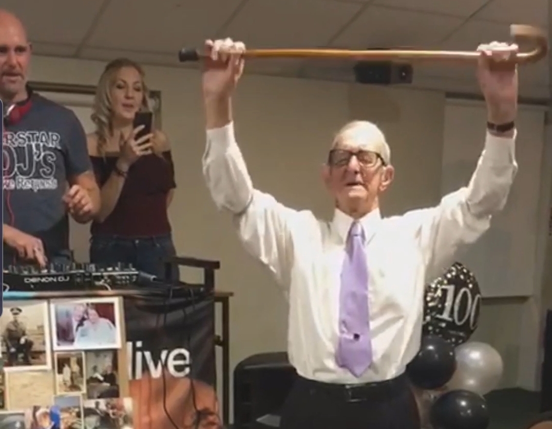 Owen Filer raises his walking stick in the air to celebrate turning 100