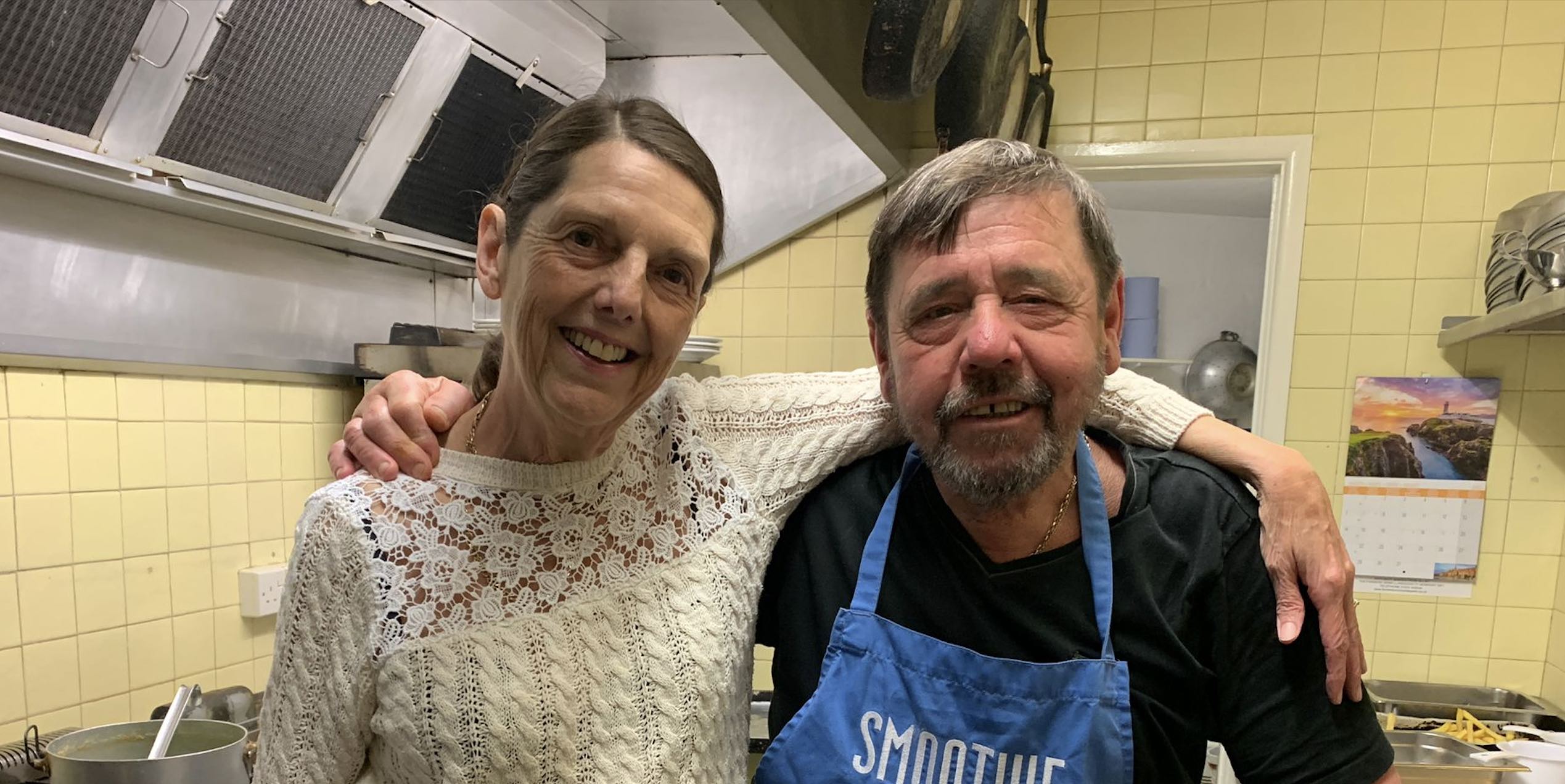 Smiling couple in pub kitchen with arms around each other