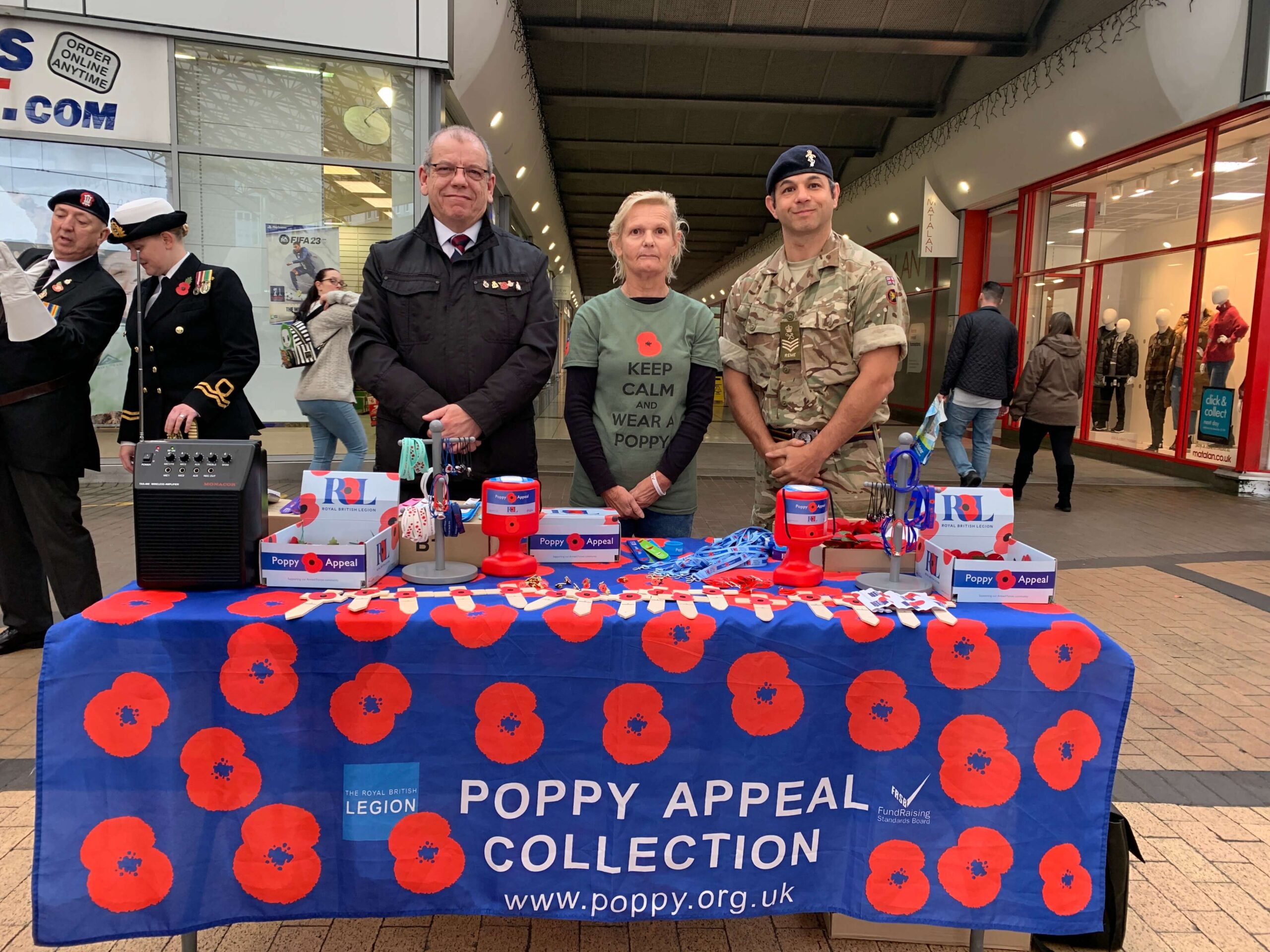 a soldier and two people by a stall selling poppies