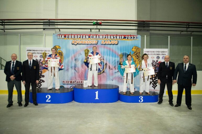 three woman on a podium holding karate trophies
