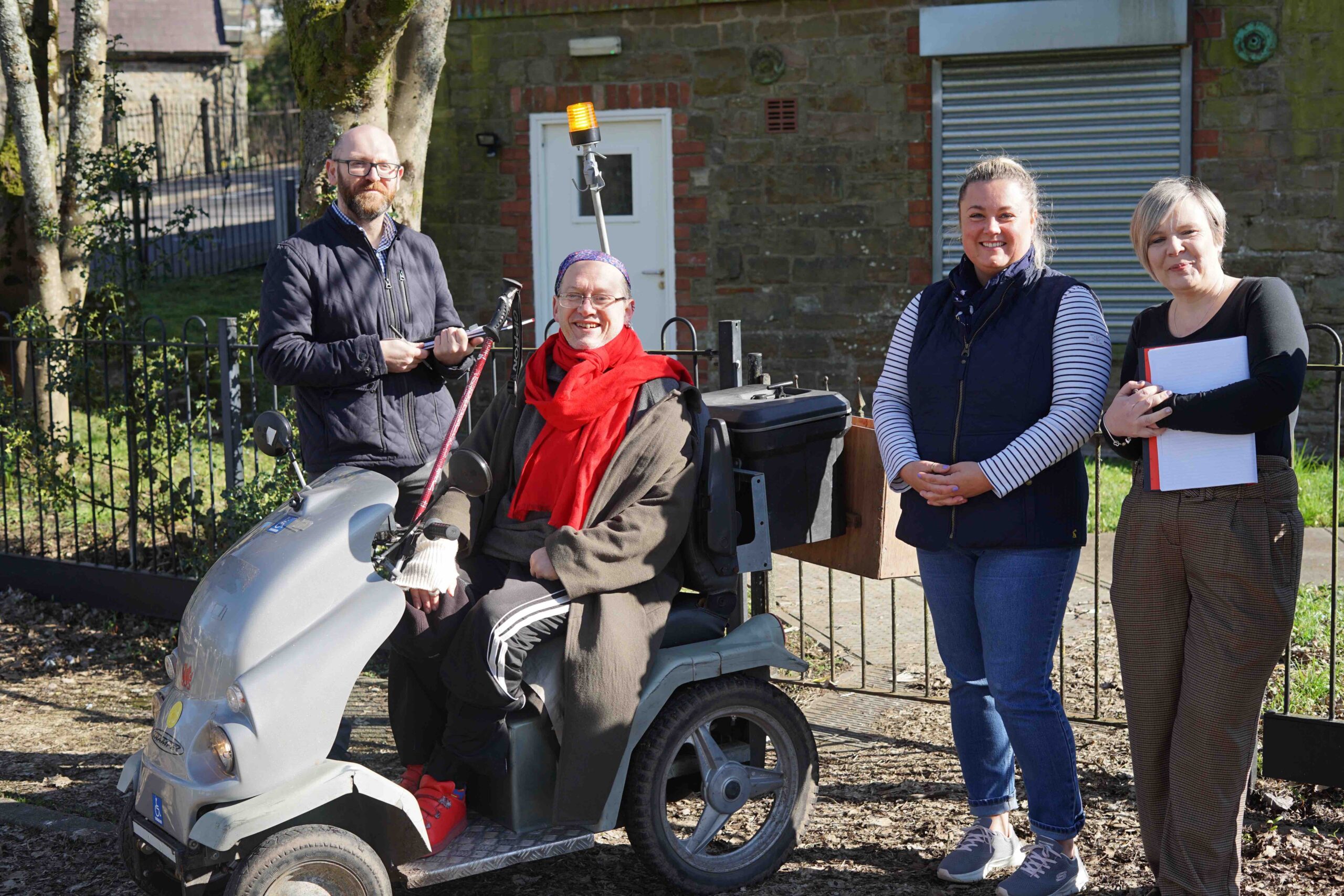 four people outside a polling station with clipboards- one woman is in wheelchair