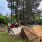 two army tents and a small group of people in a woodland