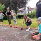 children and an adult draw in chalk on a path