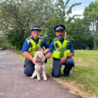 two police community support officers with a cockapoo dog
