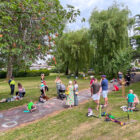 a group of adult and children stand in park while some draw in chalk on a path