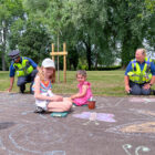 two children and two police community support officer draw in chalk on a path