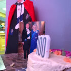 a 100th birthday cake and card next to a cardboard cut out of king Charles