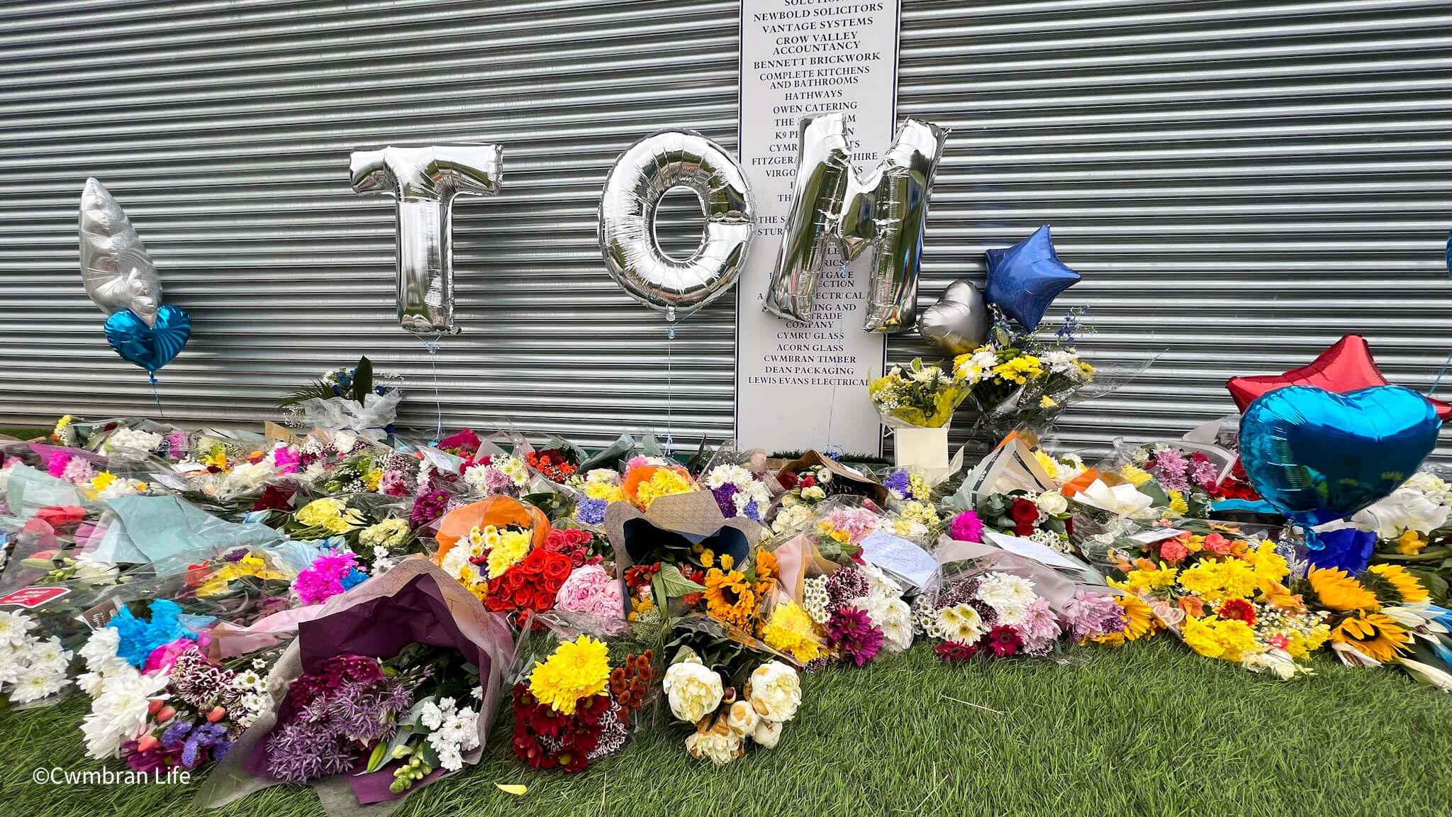 floral tributes outside a football club for a player who passed away- Silver letter balloons spell out Tom