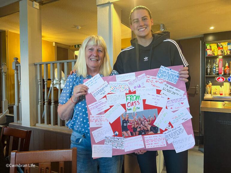 two women hold a large poster covered in good luck message