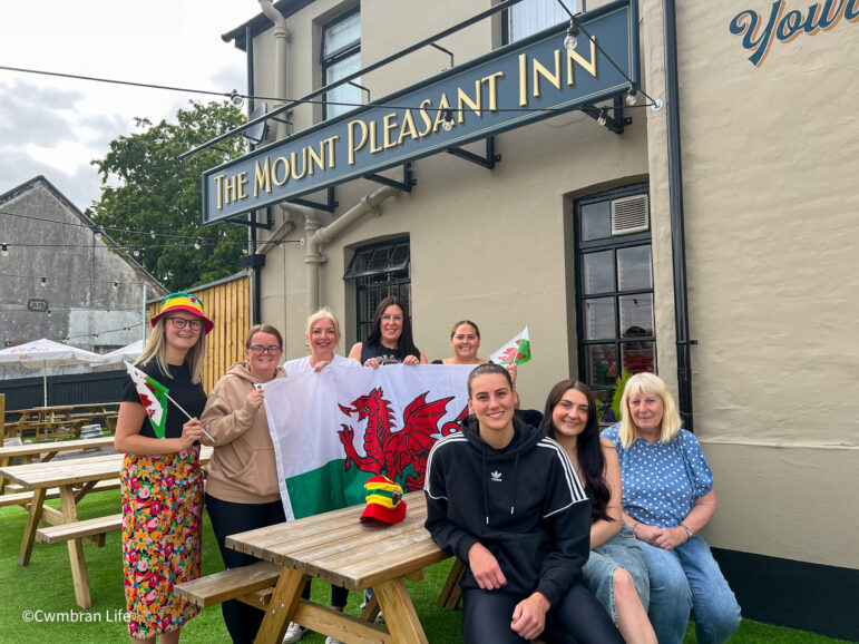 a group of women outside a pub holding a welsh flag