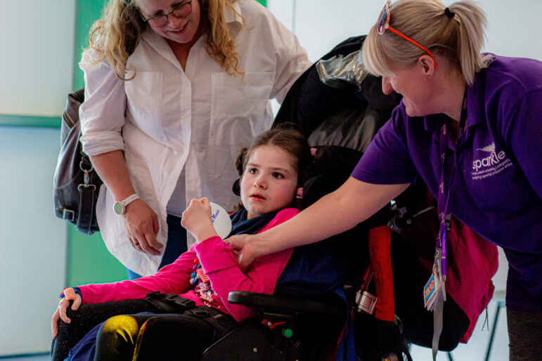 a young girl in a wheelchair with her mum and support worker smiling