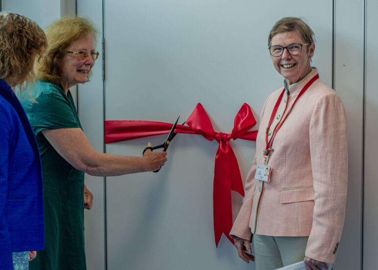 a women cuts a red ribbon with large scissors while two women watch on
