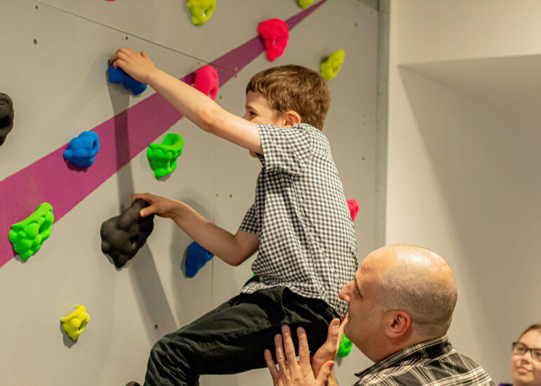 a boy on a climbing wall supported by his dad