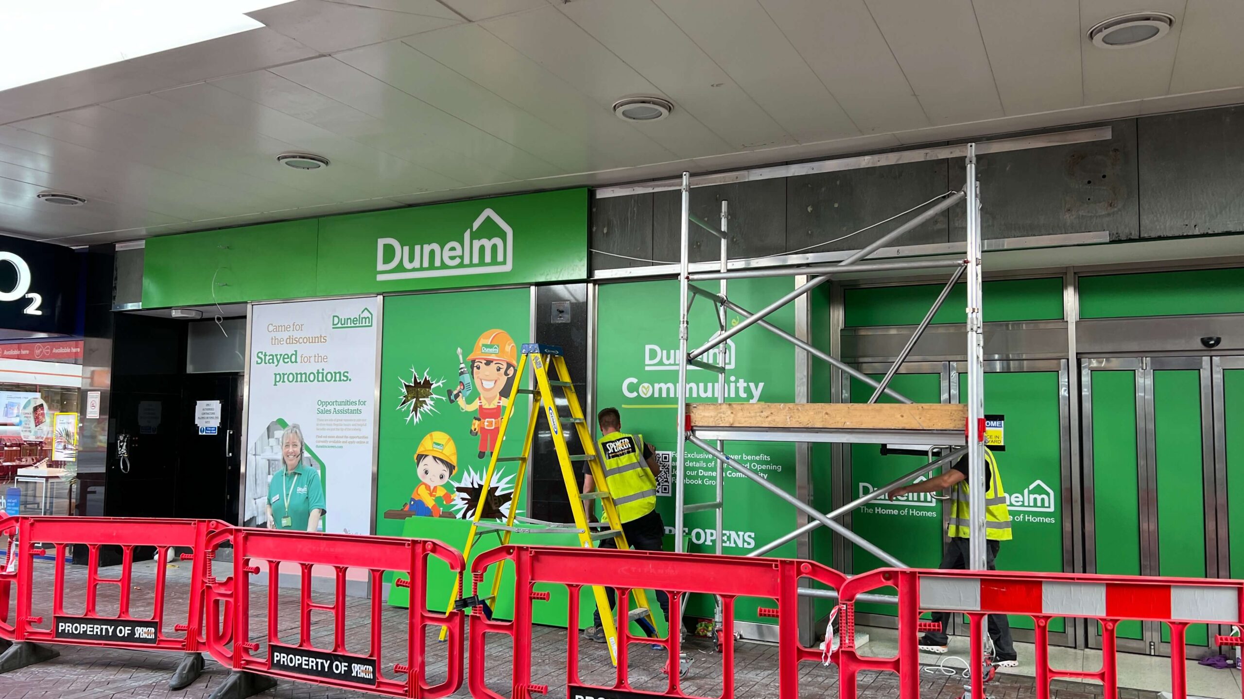 shopfitters on ladders fit a dunelm sign to a shop