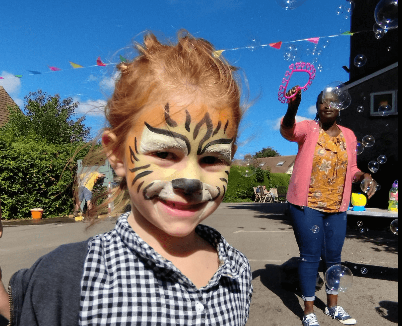 a girl with her face painted while a woman makes large bubbles behind her