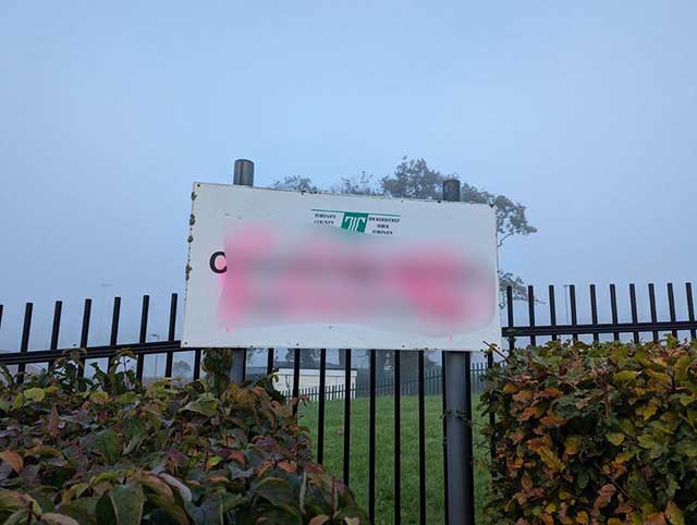 a vandalised school sign spray painted with pink paint