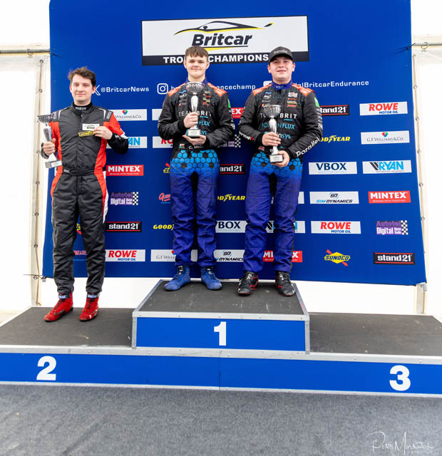 three teenage boys stood on a podium at a racing track
