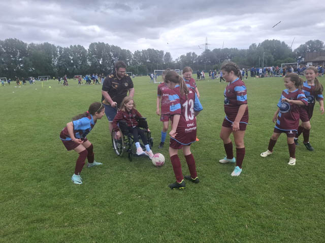 Bethany, in her wheelchair, with some of her football teammates on a pitch kicking a ball