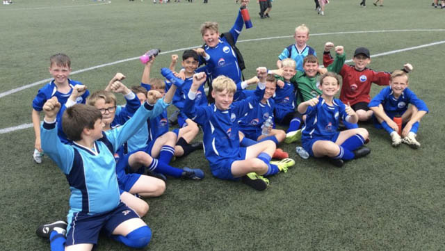 junior football team sit on floor cheering with hands in air