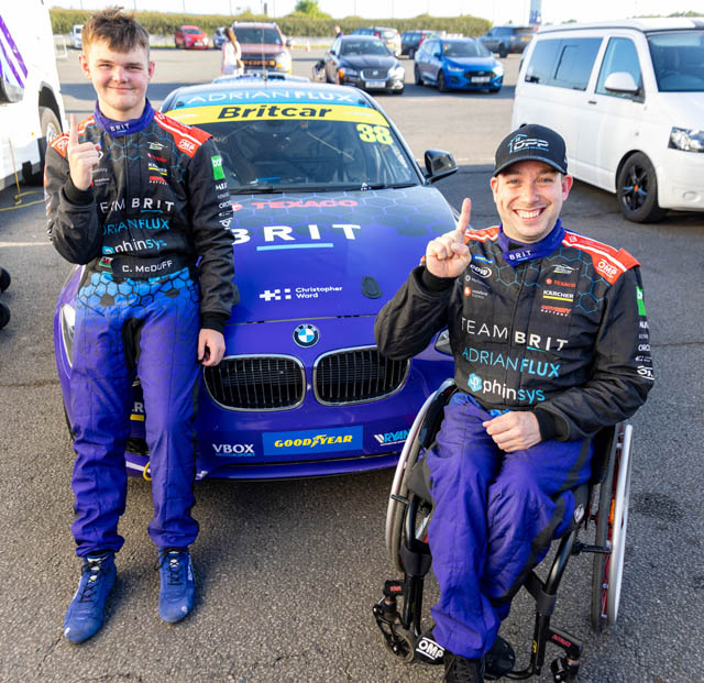 two young men by a car, one in a wheelchair