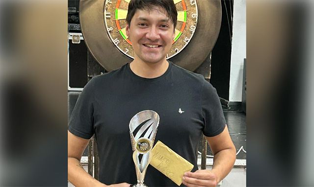 a man holds a trophy stood in front of a dart board