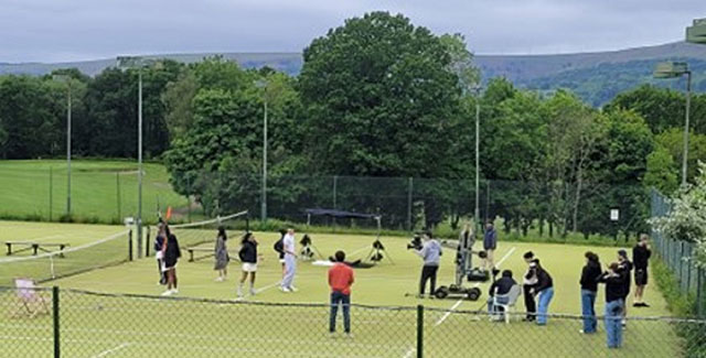 a film crew on a tennis court with a large group of people