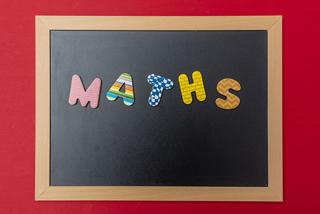 School maths concept. Black chalkboard with wooden frame, word, text maths in colorful letters, red wall background