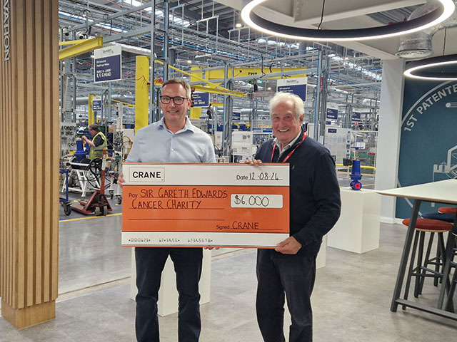 Two men hold a large charity cheque in a factory