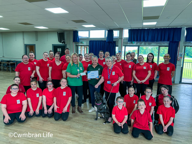 a group of 20 members of a performing arts academy present a cheque to a woman with a dog