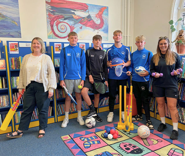 a group of people in a library holding sports kit like a cricket bat and tennis racket