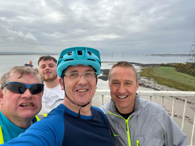 four men, one wearing a cycling helmet