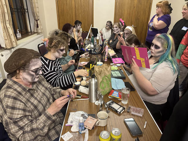 group of actors sat at table putting on make up