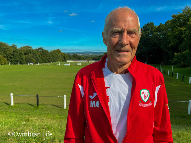 Mark wearing his red Wales tracksuit top stood by a football pitch