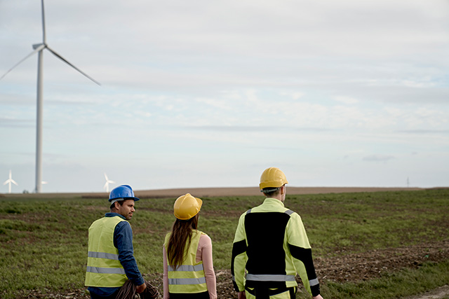 three engineers walking across wind turbine field and discussing