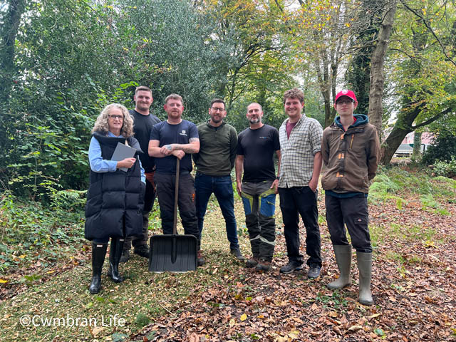 six men and a woman stood in a row in a wooded area