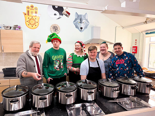 six people in a kitchen most are wearing christmas tops