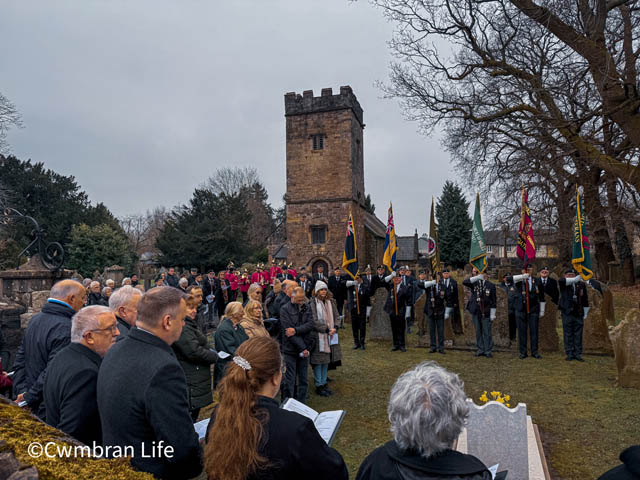 a large group of people stood around a grave in a churchyard