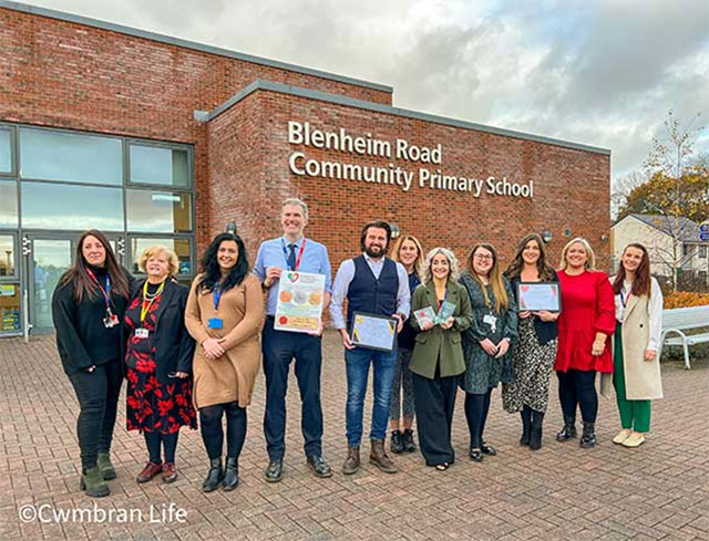 group of school staff stood outside a school with a certificate