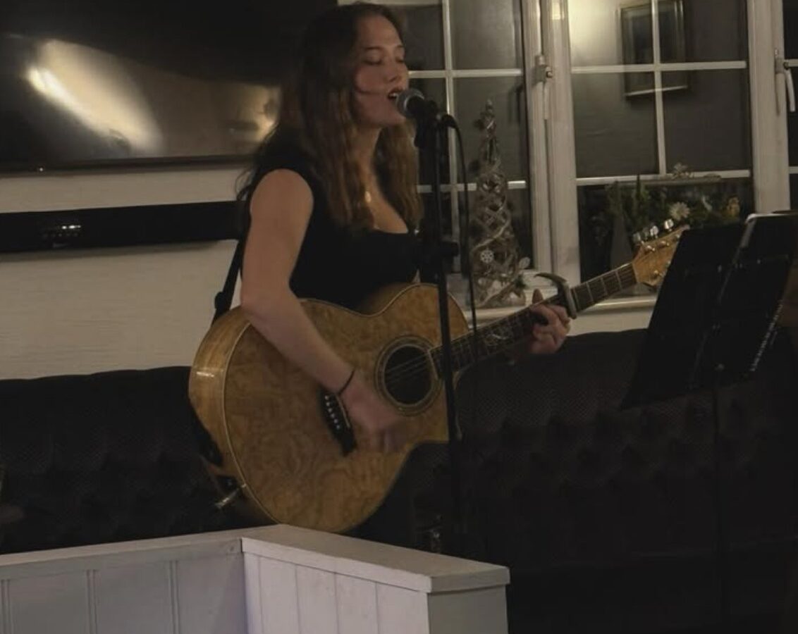 Chloe Griffin singing and playing her guitar in a pub