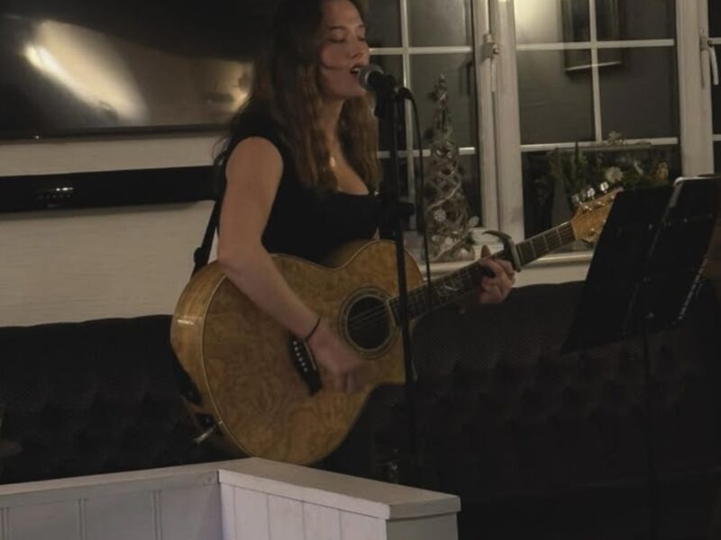 Chloe Griffin singing and playing her guitar in a pub