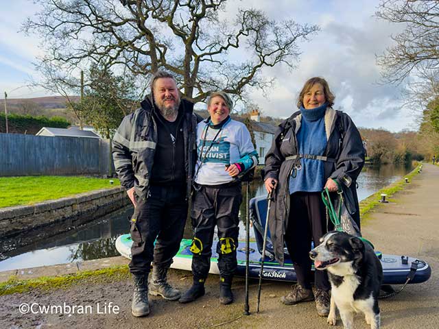 a man and two women and a dog stood by a canal