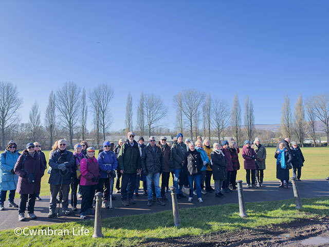 a large group of men and women smile for the camera, the sky is blue