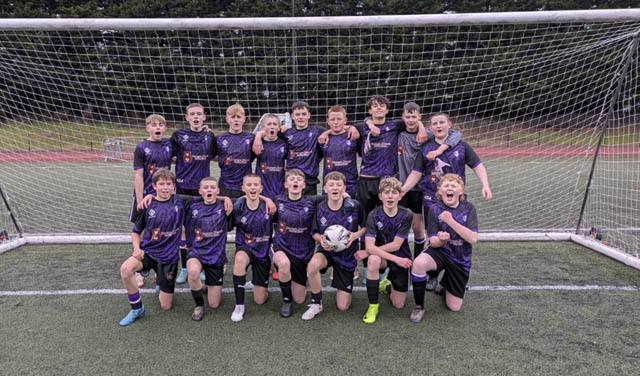 A boys football team have a photo in front of the goals