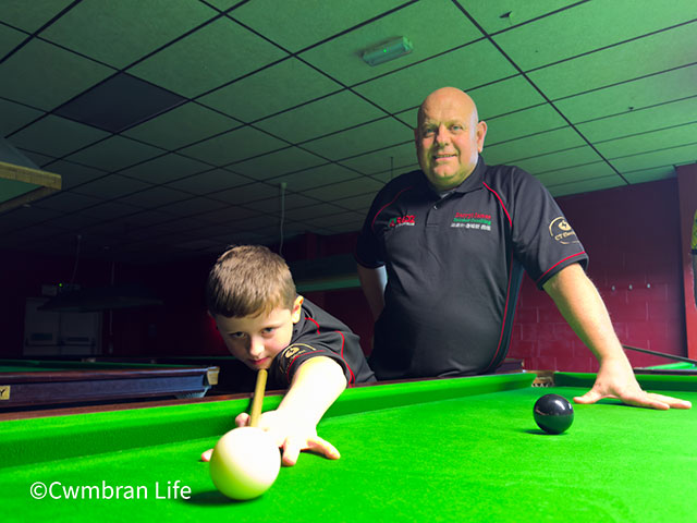 a young snooker player takes a shot watched by his coach