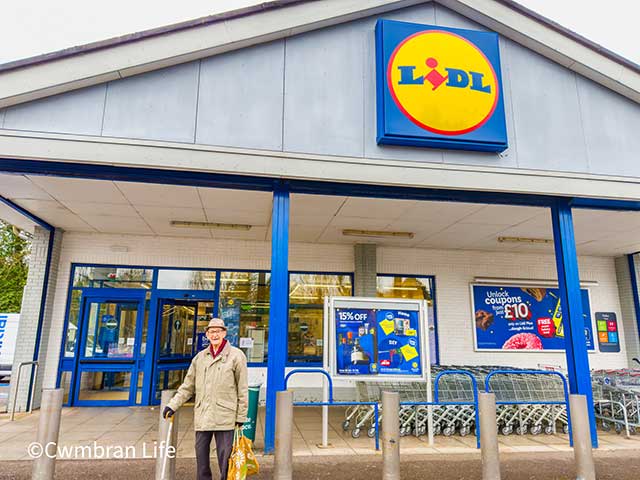 an old man stood outside a Lidl supermarket by the trollies