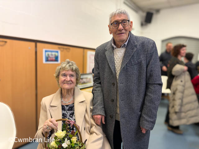 a woman sat down and a man stood next to her in a church hall