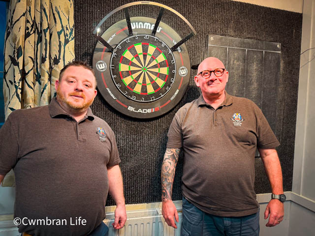 two men stood by a darts board