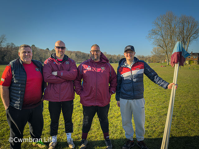 four men on football pitch smile at camera