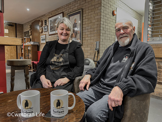 a man and woman sat at table with two coffee mugs in front of them