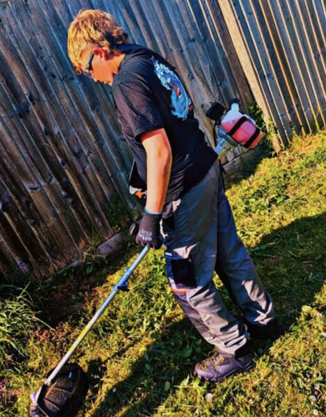a teenage boy cutsgrass with a strimmer
